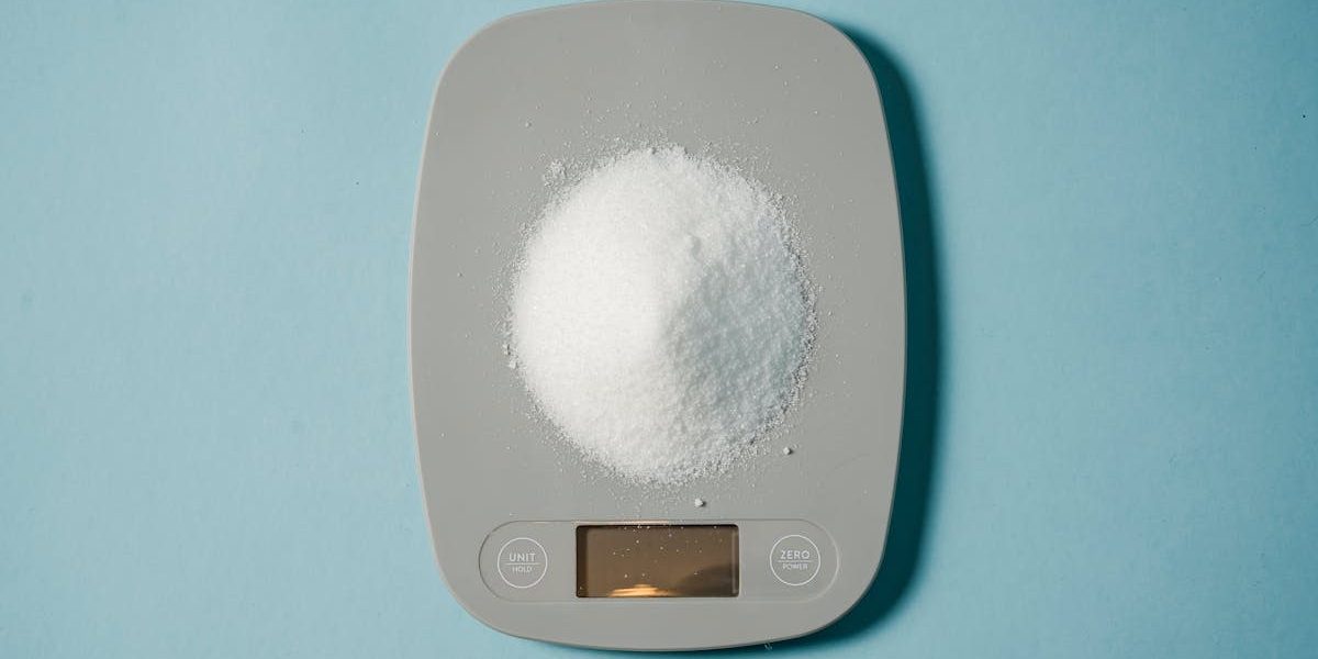 Top view of kitchen scales with electronic display measuring weight of sugar on blue background