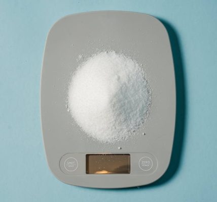 Top view of kitchen scales with electronic display measuring weight of sugar on blue background