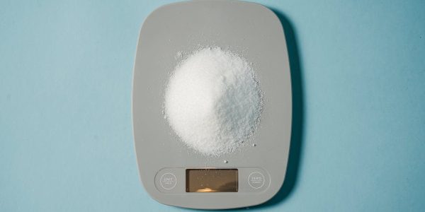 Top view of kitchen scales with electronic display measuring weight of sugar on blue background