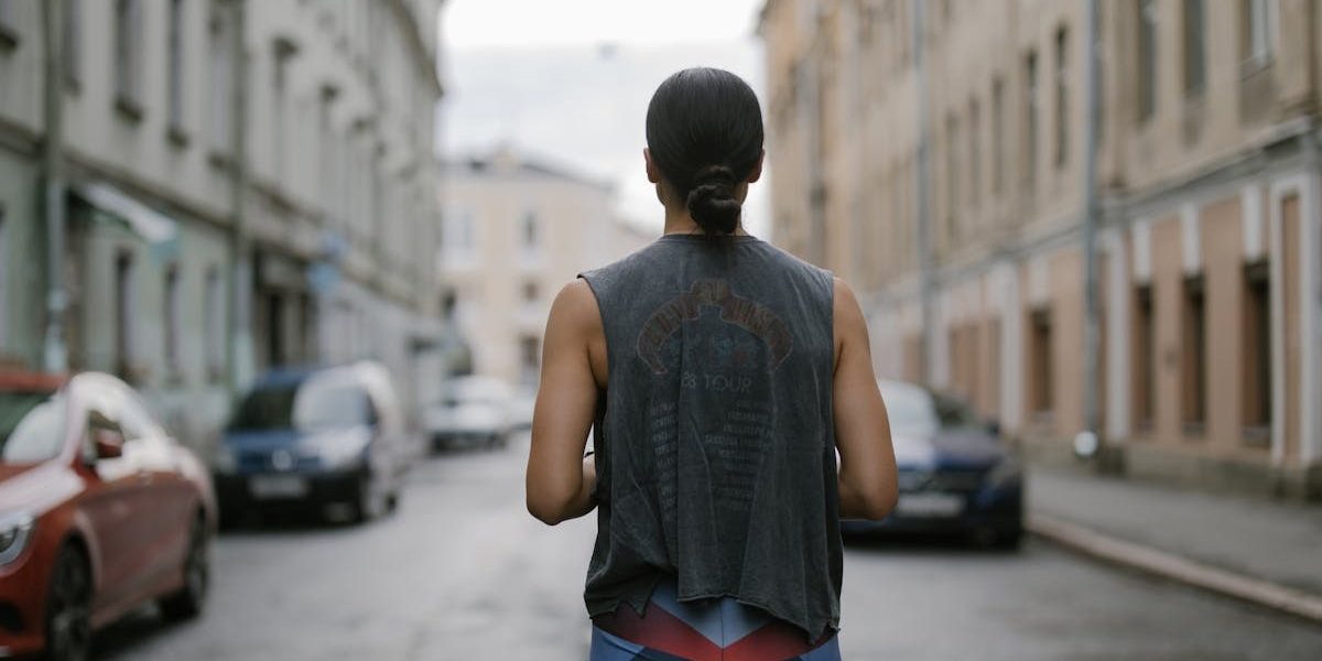 Back view of a woman in athletic wear jogging on a city street, showcasing active lifestyle.