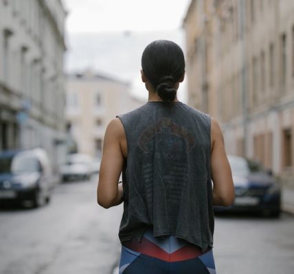 Back view of a woman in athletic wear jogging on a city street, showcasing active lifestyle.